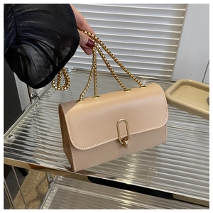 Detailed view of beige crossbody bag with gold oval metal lock and chain strap