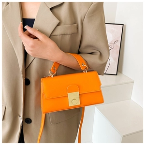 Detail of a bright orange leather handbag with gold clasp on a beige blazer background