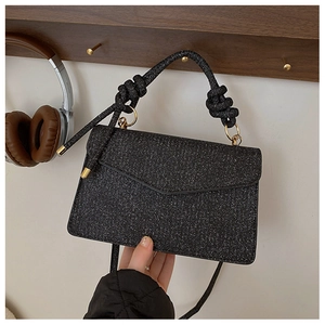 Detail of black glitter crossbody bag featuring twisted rope handle and gold metal rings