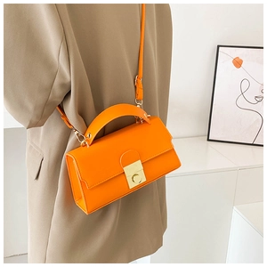 Close-up of orange leather handbag with gold twist lock on a beige coat background