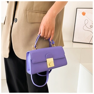 Detailed view of dark purple leather handbag with golden metal flip lock and shoulder strap