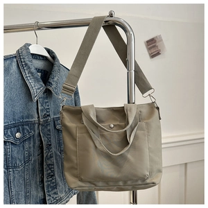 Detail of grey-green nylon tote bag with wide strap and snap button front pocket