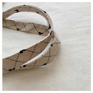 Detail of off-white corduroy shoulder strap with black diamond stitch and bow prints