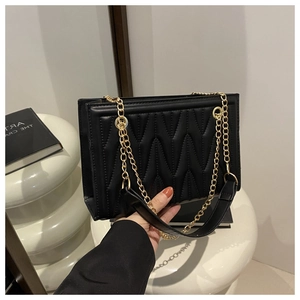 Detail of black quilted tote bag with V-shaped wave stitching and gold chain strap