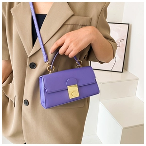Detail of purple crossbody bag with gold square twist lock worn with a khaki blazer