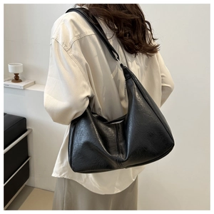 Close-up of a glossy black PU leather crescent bag worn as a shoulder bag on a model