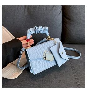 Detail of light blue crocodile texture handbag with ruched handle and golden geometric buckle