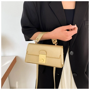 Detail of light gold minimalist handbag featuring rectangular metal lock and slim strap