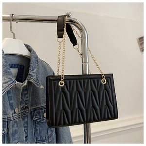 Close-up of black quilted PU leather tote featuring elegant gold chain straps and wavy stitching