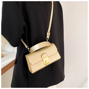 Detail of champagne gold crossbody bag with a metal square lock on a dark suit