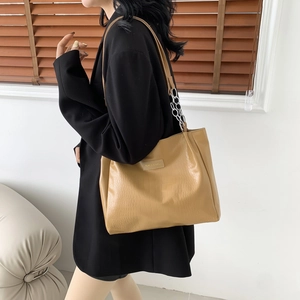 Crocodile pattern tote bag with metal chain strap worn on shoulder by model in black suit