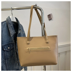 Detail view of khaki leather tote bag showing front zipper pocket and round rivet studs