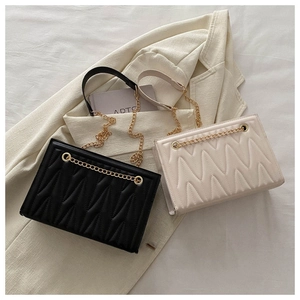 Close-up of wave-quilted PU leather bags in black and cream with golden chain straps
