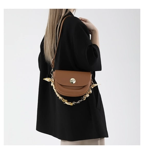 Detail of a brown saddle bag with golden clasp and silk scarf chain strap on a model