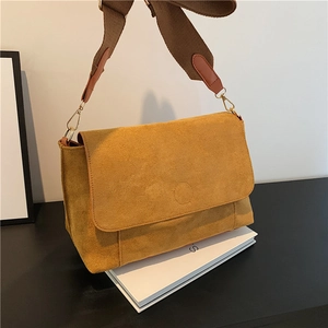 Minimalist ginger suede tote bag with a wide woven strap on a white book surface