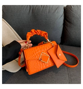 Detail of orange crocodile texture handbag with ruffled handle and mini pouch on sofa