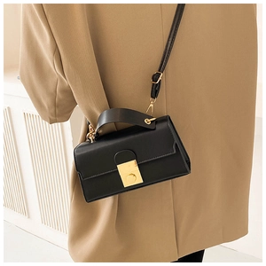 Detail showing a black structured leather handbag with a square gold clasp on a model