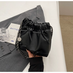 Detail view of matte black bucket bag featuring delicate bow knots and silver chain strap