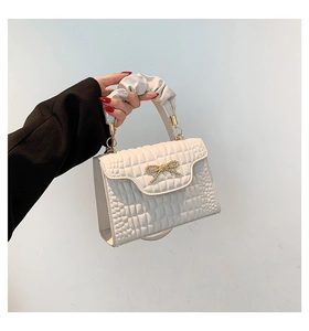Close-up of white embossed square bag featuring a gold bow buckle and pleated handle