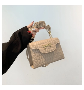 Detail of beige faux crocodile leather bag with bow hardware and cloud handle