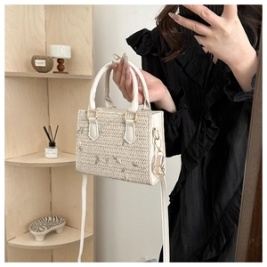 Detail of white woven handbag featuring floral embroidery and gold metal hardware