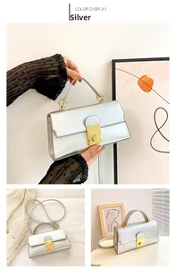 Silver handbag featuring a rectangular profile with golden ring hardware and detachable strap