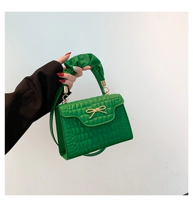 Close-up of green crocodile pattern handbag featuring a gold bow and ruched handle