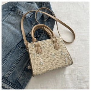 Detail of floral embroidery on a beige woven straw crossbody bag over a white plaid fabric