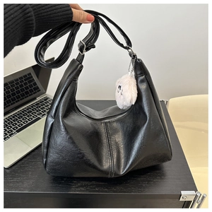 Detail of black PU leather tote bag with wide strap and white cat plush charm accessory