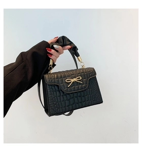 Close-up of black crocodile pattern handbag with golden bow metal and pleated handle
