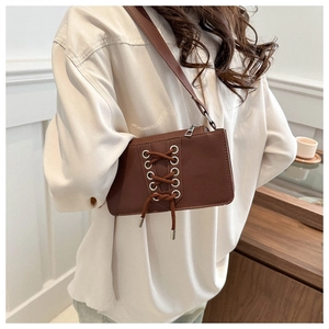 Détail du sac bandoulière marron foncé en similicuir avec œillets métalliques et lacets
