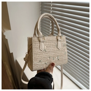Detail of cream straw bag featuring green floral embroidery and dual top handles