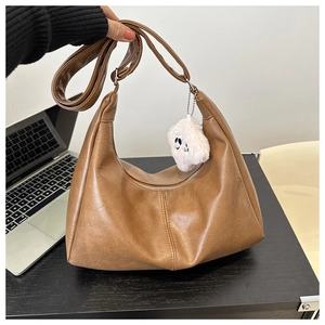 Close-up of brown PU leather crescent tote bag with white ghost charm on desk