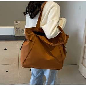Detail of a brown tote bag with black drawstring closure on a casual shoulder strap