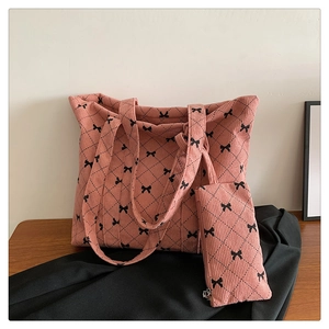 Close-up of pink corduroy tote bag and pouch set with black bow patterns on wooden table