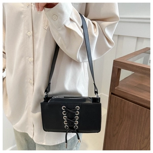 Détail du sac à bandoulière en cuir verni noir avec laçage corset et œillets argentés