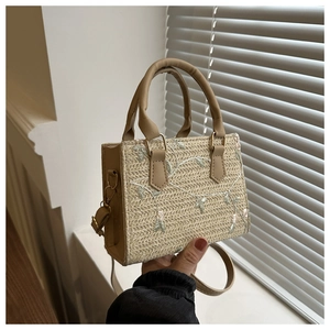 Detail of floral embroidery on a woven straw handbag with light brown leather trim