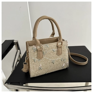 Close-up of woven straw bag with floral embroidery and leather handle on a chair