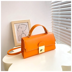 Detail of bright orange rectangular handbag featuring a gold square metal lock and strap