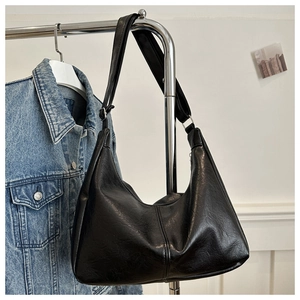 Macro detail of the sleek black faux leather texture and silver hardware of the hobo bag