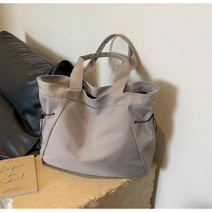 Detail of taupe waterproof nylon tote bag with side drawstrings on a stone base