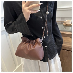 Detail of a brown pleated cloud bag with a silver chain strap and metallic ball accent
