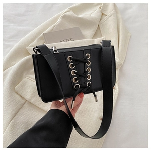 Détail du sac à bandoulière en cuir verni noir avec œillets argentés et design à lacets