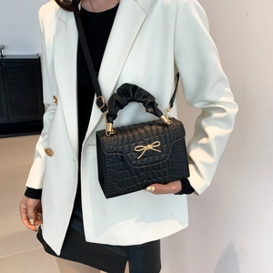 Black textured shoulder bag with golden bow and pleated handle worn with white blazer