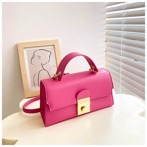Detail of a bright magenta minimalist handbag with a golden square metal lock and smooth leather
