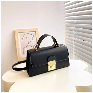 Detail view of black faux leather handbag with golden metal buckle on elegant white display