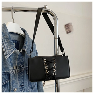 Détail du sac baguette en cuir verni noir avec œillets argentés et laçage élégant