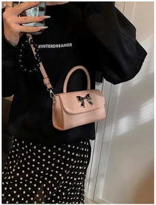 Close-up of pink patent leather crossbody bag with golden metal bow and bead chain detail
