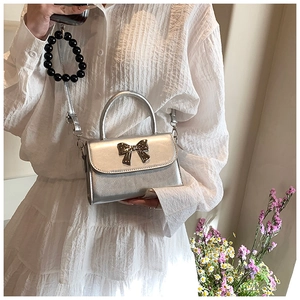 Close-up of metallic silver crossbody bag with a large bow-shaped hardware ornament