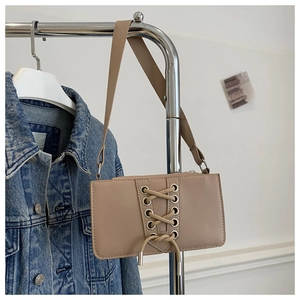 Détail d'un sac à bandoulière beige avec laçage et œillets sur un cintre métallique